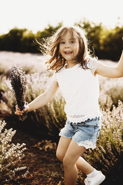 嬉戏可爱的小女孩看着相机笑着在夕阳下的一片生态花卉地里玩耍女孩欢乐放松