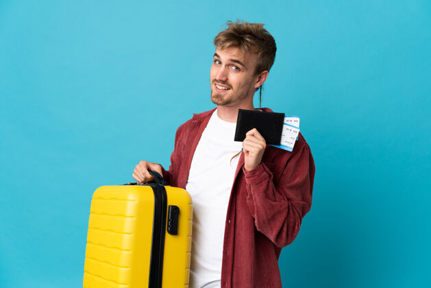 年轻年轻英俊的金发男人带着手提箱和护照在蓝色的度假中与世隔绝年轻旅行男性