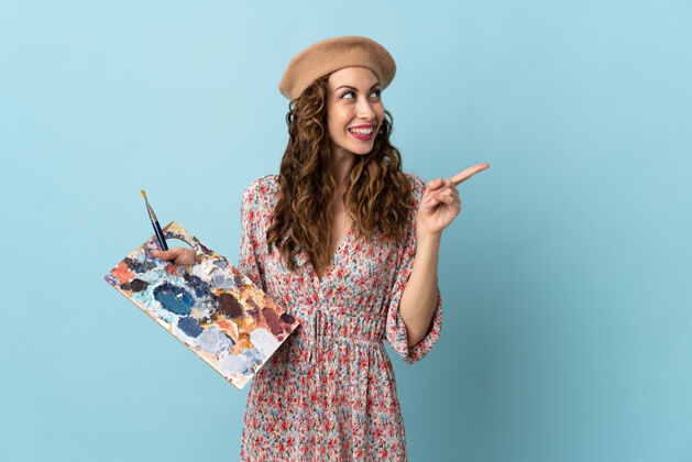 绘画年轻的艺术家女孩拿着一个蓝色的调色板 打算实现解决方案 同时举起一个手指专业怀疑女人