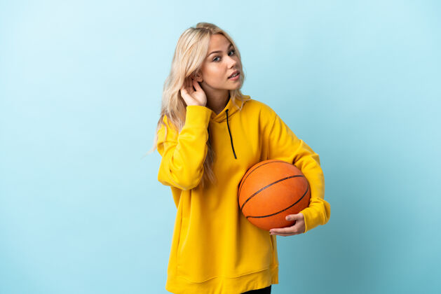 比赛一个年轻的俄罗斯女子在蓝色的场地上打篮球 手放在耳朵上听东西耳朵人声音