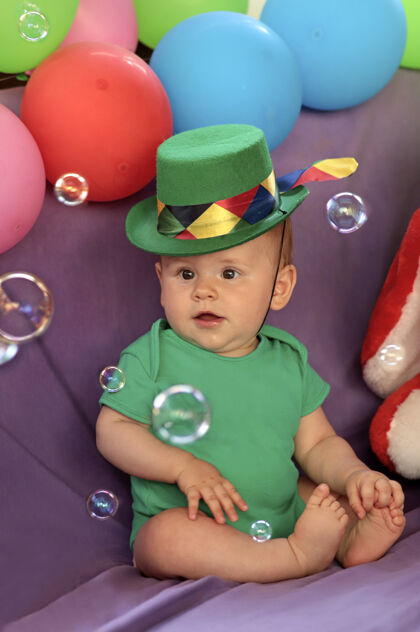 宝贝宝宝坐在一个有趣的节日气氛与气球和看肥皂泡帽子男孩孩子
