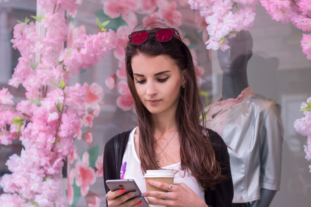 休闲一个年轻漂亮的女人站在一个店面旁边 一边端着咖啡 一边盯着电话购物欧洲欢呼