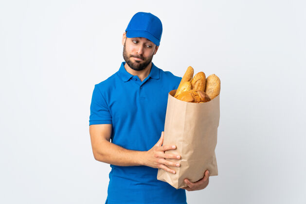 工人送货员拿着一袋面包 隔离在白色背景上 表情悲伤压力面包专业