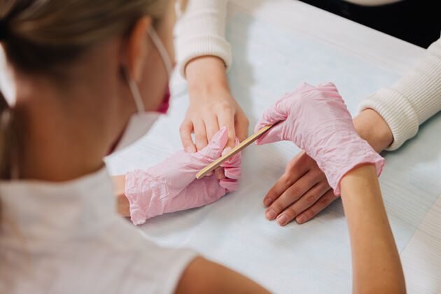 手修指甲的过程一个戴着粉色橡胶手套的师傅用指甲来修指甲文件.female把手收起来橡胶手指美容