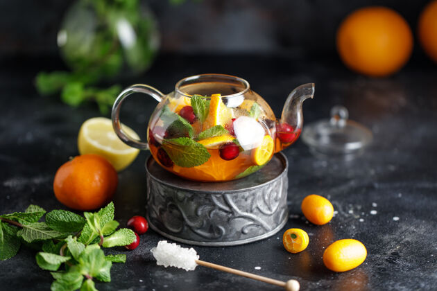 冷的水果茶配薄荷 橙子和红莓 背景为深色石头一杯热茶叶子甜的茶壶