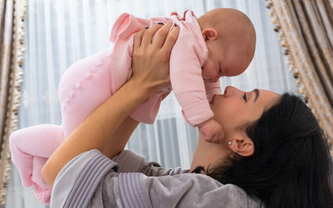 信任可爱的母亲和她的小女婴一起玩 把她高高地举起来 这是一幅室内的特写柔美肖像婴儿封闭母性