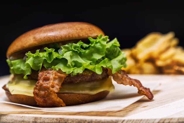 肉类美味的芝士汉堡 配上培根和生菜 放在一个新鲜的硬面包卷上 放在一张纸上 作为快餐或酒吧午餐包子切达咖啡馆