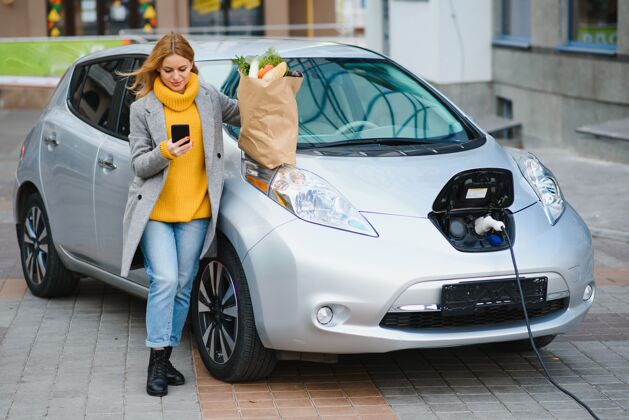 汽车时尚女士买完产品后拿着购物袋正站在充电的电动车旁环保户外自然