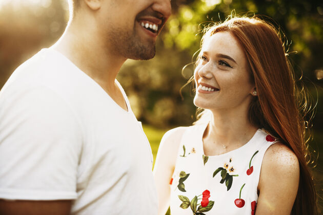 女性一位长着雀斑和红色长发的可爱年轻女性的侧视图 在日出和树木的映衬下微笑着看着她的男朋友女人阳光家庭