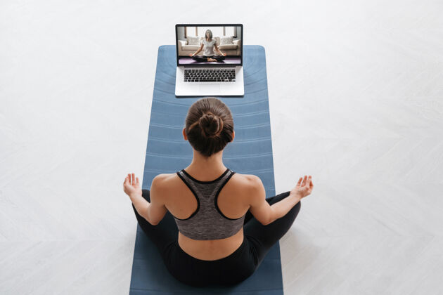 减肥顶视图年轻的运动女性使用笔记本电脑训练哈他瑜伽与虚拟教练 做sukhasana活动教程活动