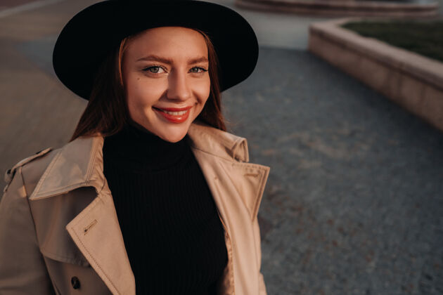 外套一个穿着米色外套 戴着黑帽子的时髦年轻女子街头女人的街道时尚.秋季服装.城市风格姿势时尚脸