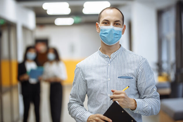 男人优雅的商人戴着医用口罩站在办公室走廊里 手里拿着一块药片文件距离商业男人