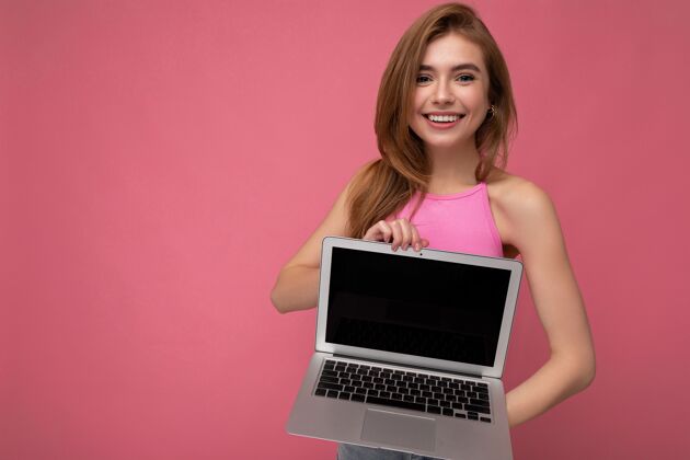 自由职业者美丽微笑的金发女郎手持笔记本电脑 空着显示器 身穿粉色短上衣快乐学习网站