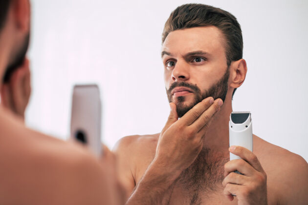 感性英俊的年轻人在街上刮胡子浴室.肖像一个时髦的裸体胡须男人在家里的镜子里检查他的脸男性理发师卫生