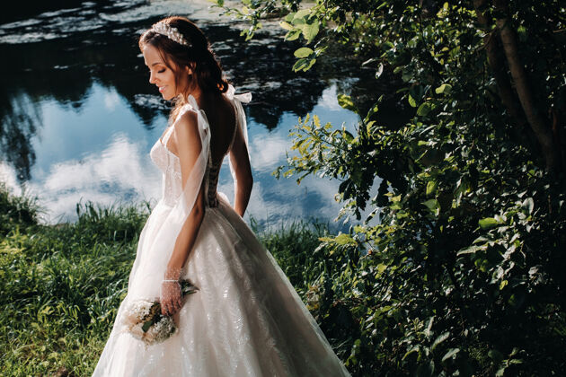 女人一个优雅的新娘在一个自然公园里穿着白色的裙子和一束花束的肖像石头立场礼服