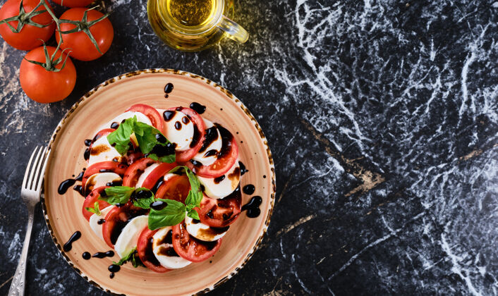 晚餐西红柿和马苏里拉 意大利卡普雷斯西红柿沙拉 马苏里拉奶酪 罗勒香醋和橄榄油.深色大理石墙 顶视图 素食风味生物叉子