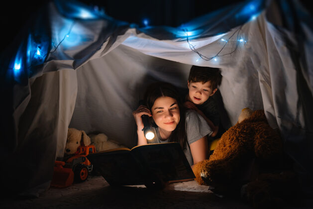 父亲幸福家庭母子俩在帐篷里用手电筒看书主页.家庭概念教育男性小
