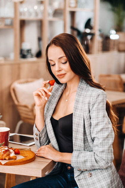 水果一个女人正坐在咖啡馆里吃草莓一个女孩手里拿着草莓在咖啡馆里模特维生素快乐