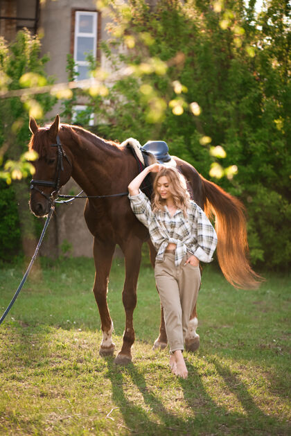 动物美丽的姑娘牵着她的马和美丽温暖的夕阳在春天的森林里青少年金发草地