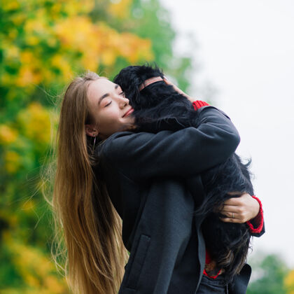 拥抱秋天公园里日出时分 一位年轻迷人的女士抱着她的腊肠狗在户外成人微笑年轻