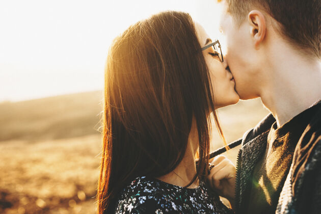 女朋友一位戴着时髦眼镜的迷人年轻女士站在阳光明媚的乡村 亲吻着匿名男友的脸颊戴女人在乡下吻男朋友休闲在一起感情