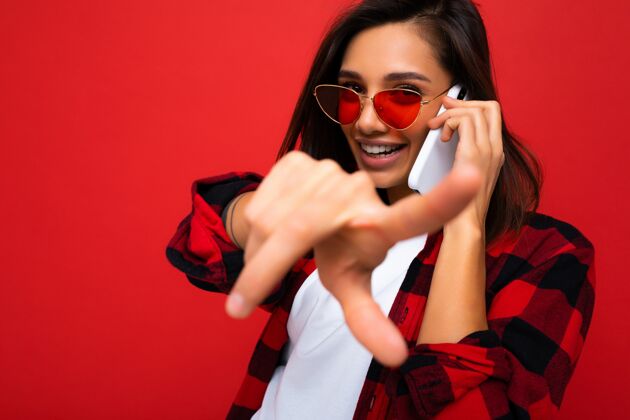 手机特写美丽快乐的年轻黑发女子穿着时尚的红色衬衫白色t恤和红色新鲜沟通手势