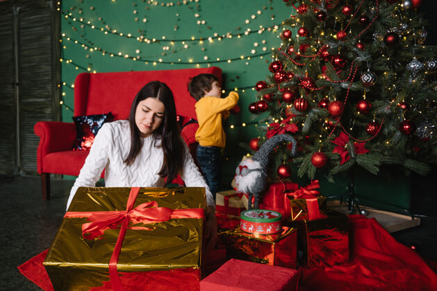女孩年轻美丽的母亲带着可爱的儿子在圣诞树旁礼物快乐圣诞节快乐盒子父母