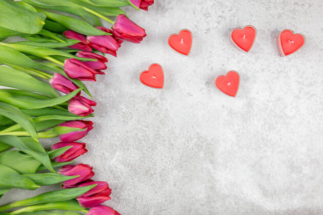 植物美丽的红色郁金香和红蜡烛的花束 在灰色的混凝土上形成一个心形情人节爱五颜六色