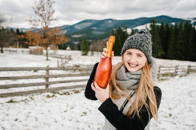 饮料美丽的女人拿着一瓶香槟在冬天的背景下山女孩在下雪的冬天 进来走走自然.旅行还有假期概念.假期冬季肖像火花山