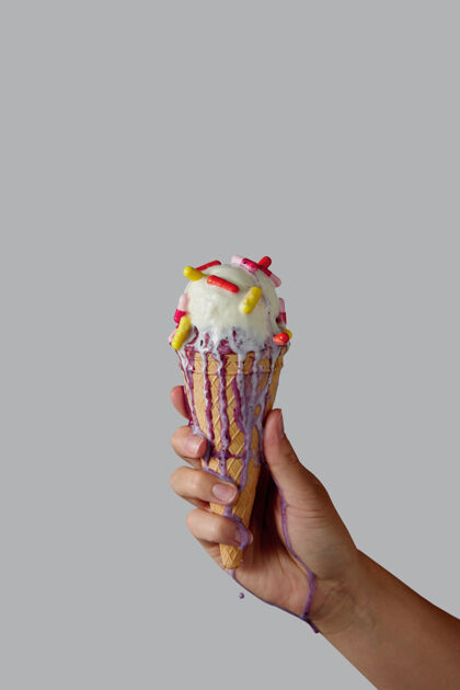 奶油一个女人的手拿着融化的香草冰淇淋和多色片在华夫饼圆锥体上的灰色墙.副本文本空间冷藏奶油球