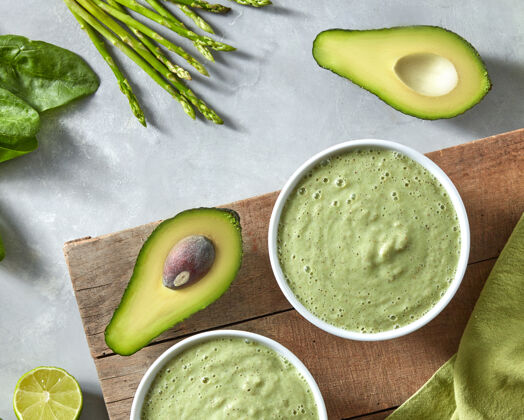食物自制的绿色健康冰沙来自菠菜 鳄梨和芦笋 放在木板上 绿色餐巾放在水泥墙上叶子营养蔬菜