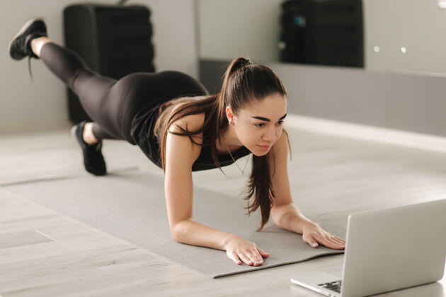 成人迷人的健美女士一边做瑜伽板一边看网上教程笔记本电脑.培训在学习中运动位置相机