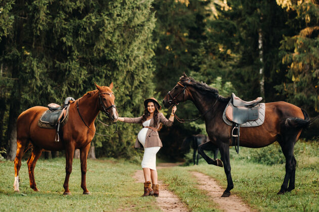 怀孕在大自然的森林里 怀着大肚子的女孩戴着帽子在马旁边快乐自然腹部