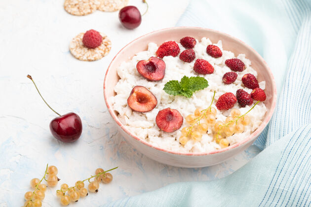 草莓米片粥加牛奶和草莓放在白色混凝土表面和蓝色亚麻织物的陶瓷碗里谷类混凝土浆果