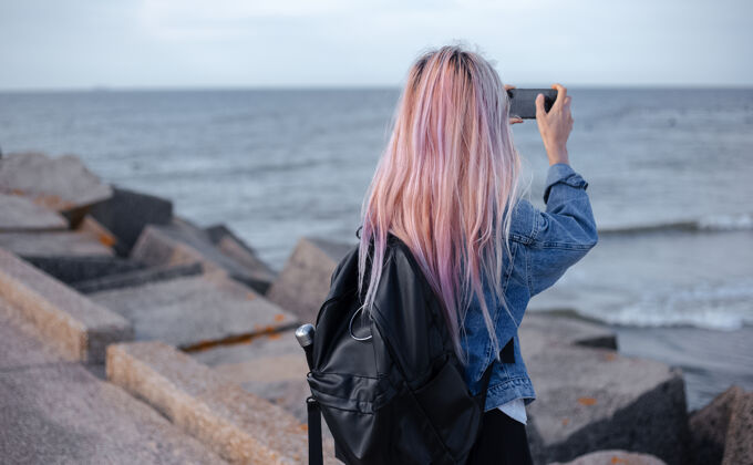 感性粉色头发 穿着牛仔夹克和黑色背包的年轻女孩的后视图海岸女性肖像
