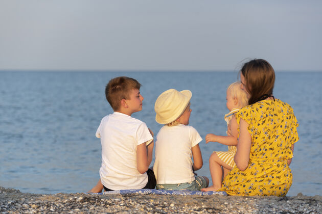 爱带着三个孩子的年轻母亲正在床上休息海边后面视图.族在海边度假小两个妈妈