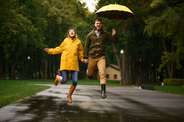 关系一对幸福的情侣像孩子一样在公园里跳跃 夏日多雨戴曼雨伞下的女人 散步路上的浪漫约会 小巷里的潮湿天气女性夫妇一对