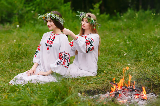 女性仲夏二穿着斯拉夫衣服的女孩在火炉旁的头发上编辫子时尚服饰自然