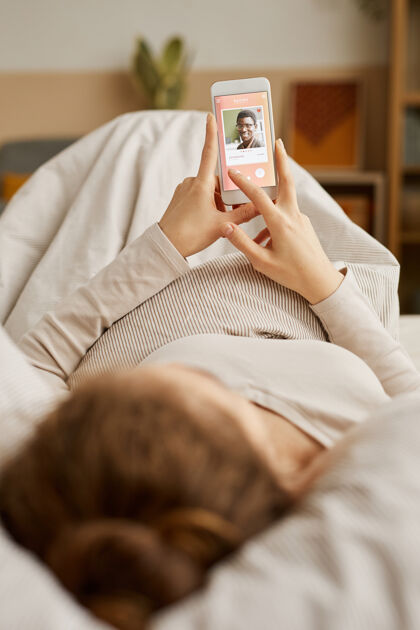 约会年轻女子躺在床上 一边看手机上的照片 一边在家休息家庭生活舒适家庭房间