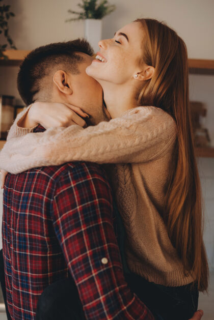 拥抱一对可爱幸福的夫妇的肖像 一个男人抱着他的胳膊 他的女朋友亲吻她的脖子 而她在家里闭着眼睛笑着光男人亲吻