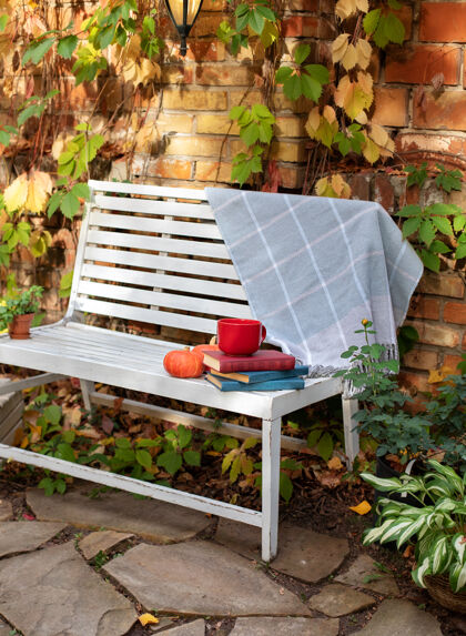 咖啡馆秋天的白板凳花园.后院花园里种植装饰性的绿色植物菊花堆一堆书 一杯茶 格子布和南瓜躺在木凳上书野餐夏天