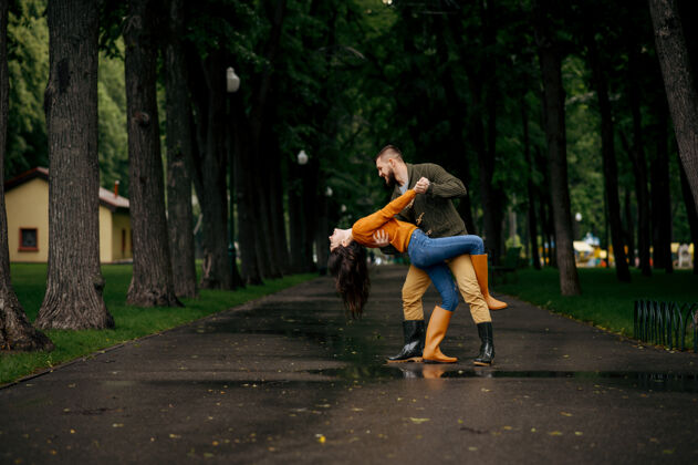 女性夏日雨中公园里快乐的情侣跳舞戴曼雨中的女人在雨伞下拥抱 散步路上的浪漫约会 巷子里的潮湿天气季节情人保护