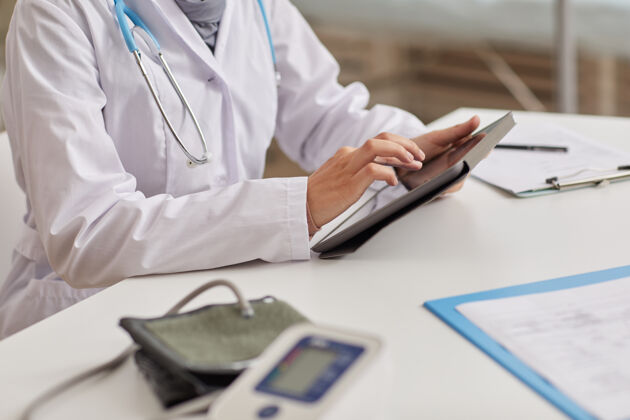 药品一个穿着白大褂的女医生坐在工作场所 在数字平板电脑上在线工作的特写镜头女医生职业专业知识