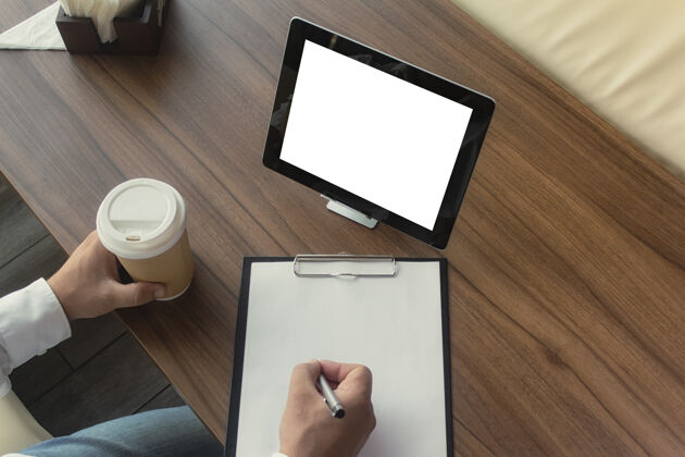 金融一位身穿白衬衫 手里拿着一台数字平板电脑的商人在伦敦签署了一份合同办公室.工作场所一杯咖啡 一份文件 一支笔放在木桌上平板电脑设备数字