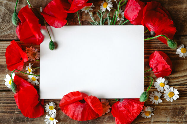 花一张白色的纸 上面有红色的罂粟花和雏菊 在棕色的木头上罂粟花平铺花