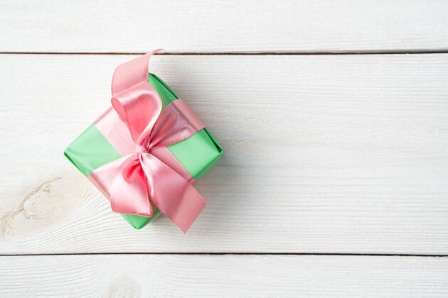 周年纪念一个绿色包装的小礼盒 白色木质背景上有一条粉红色的缎带礼品盒羽毛丝带