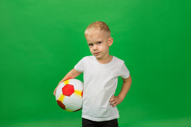 男性一个穿着白色t恤的小男孩足球运动员的肖像 绿色的是一个足球运动员活动学校