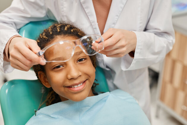 女孩当牙医戴上护目镜时 年轻女孩在前面微笑的画像病人快乐牙医办公室