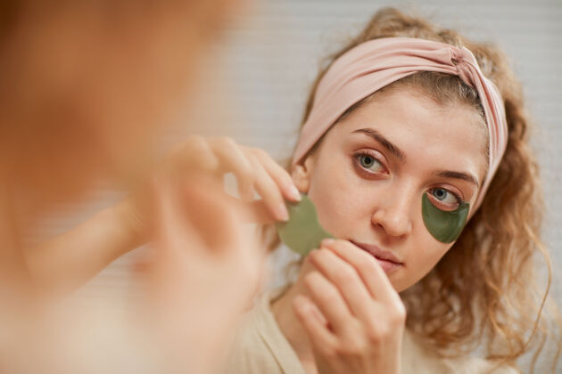 女性化年轻女子一边看镜子 一边用眼罩敷眼睛美容微笑家庭浴室