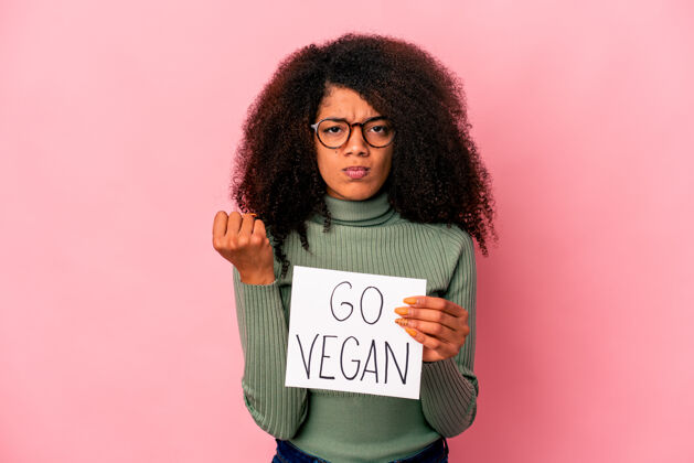 女人年轻的非洲裔美国卷发女子举着一个素食主义者的标语牌显示拳头 咄咄逼人的面部表情女性拳头绿色